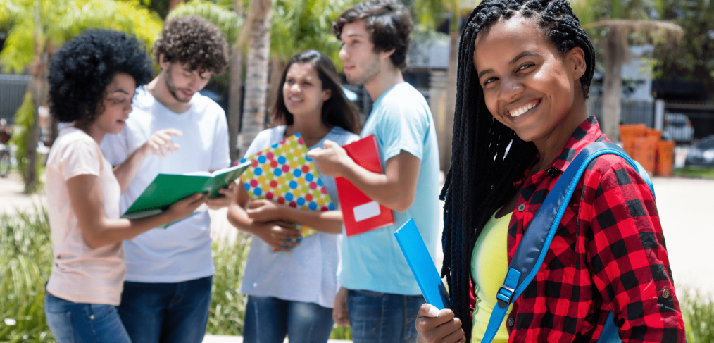 college students outdoors holding notebooks, smiling, wearing backpacks