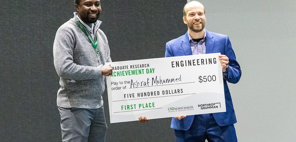 Ashraf Mohammed holds his first place check for $500 standing alongside Jason Hicks, systems engineering manager at Northrop Grumman. Photo by Walter Criswell/UND Today.