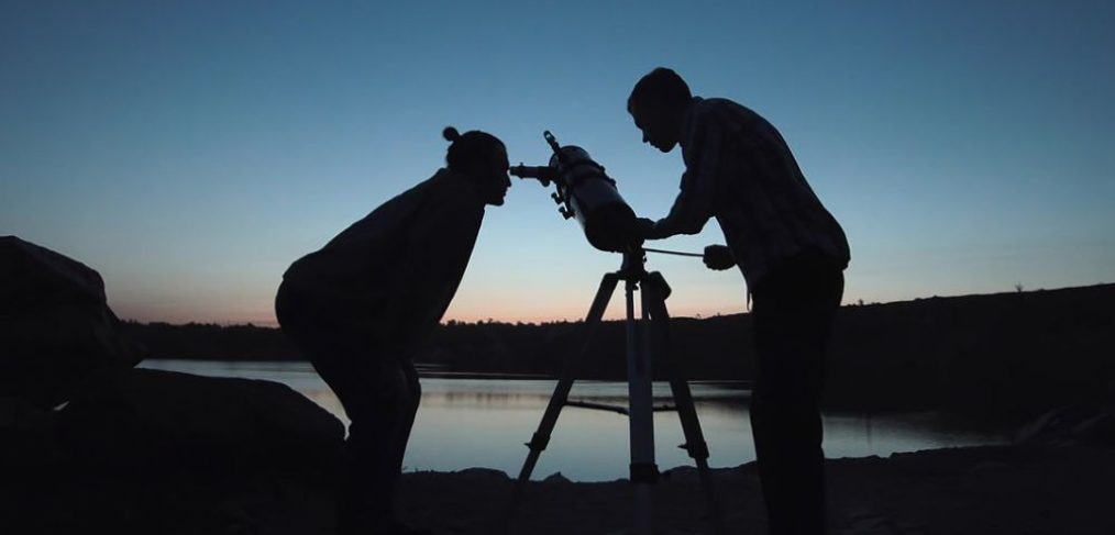 Silhouette of two people looking through telescope