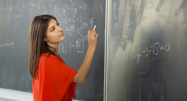 Student writing calculus equations on a blackboard with chalk